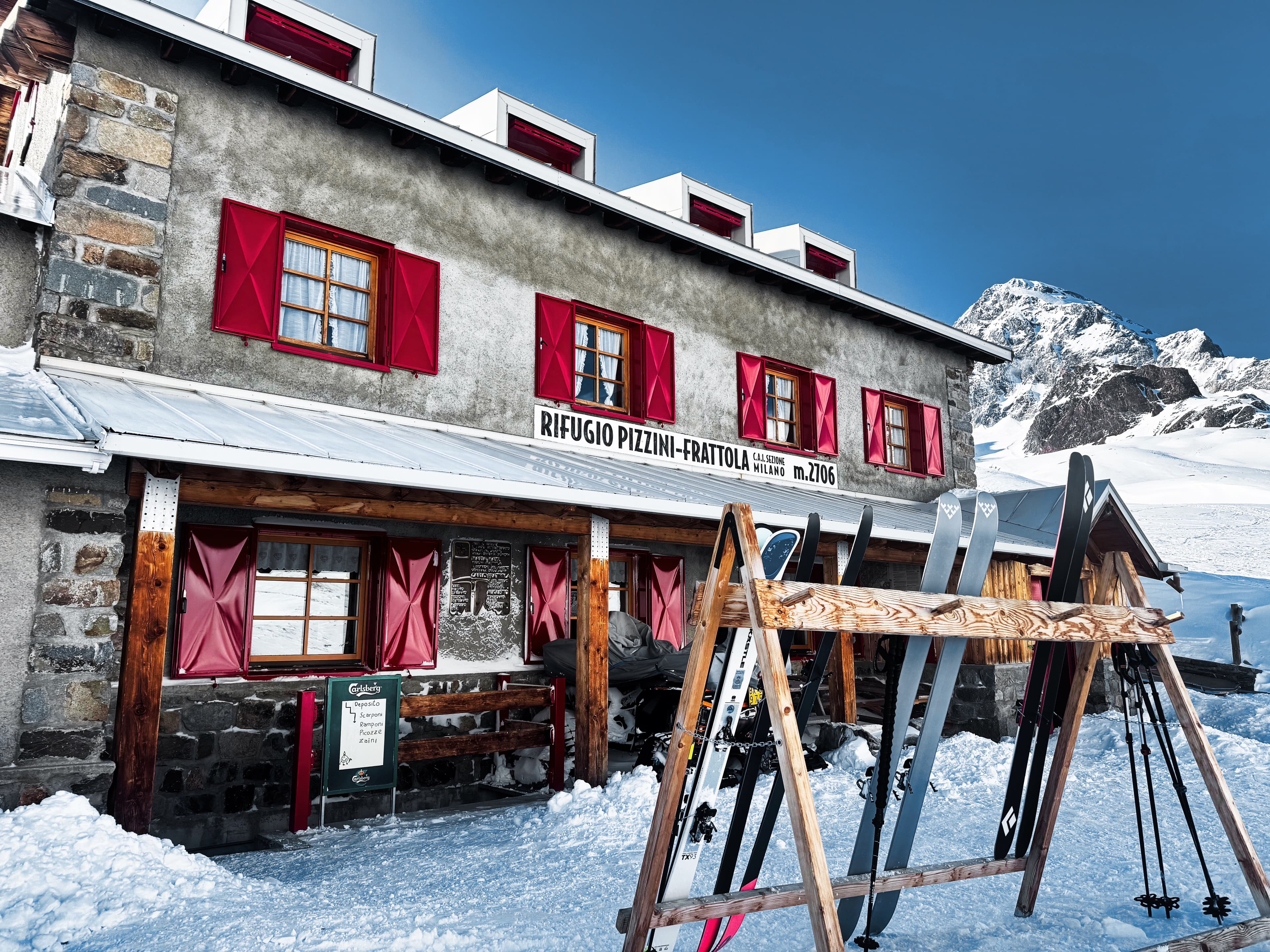 Rifugio Pizzini-Frattola at 2706m with red shutters and ski rack