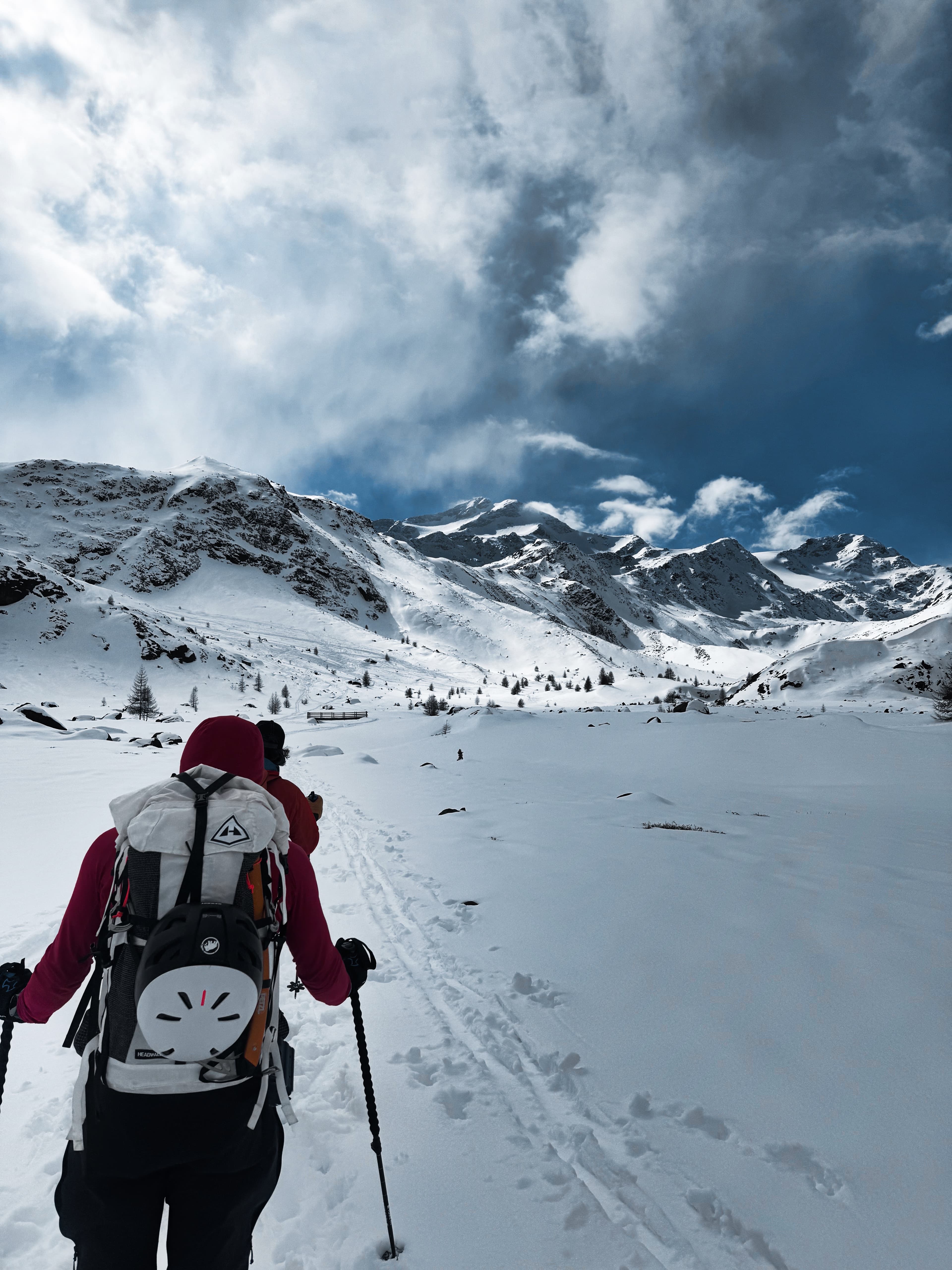 Skier skinning toward snow-covered peaks under dramatic clouds