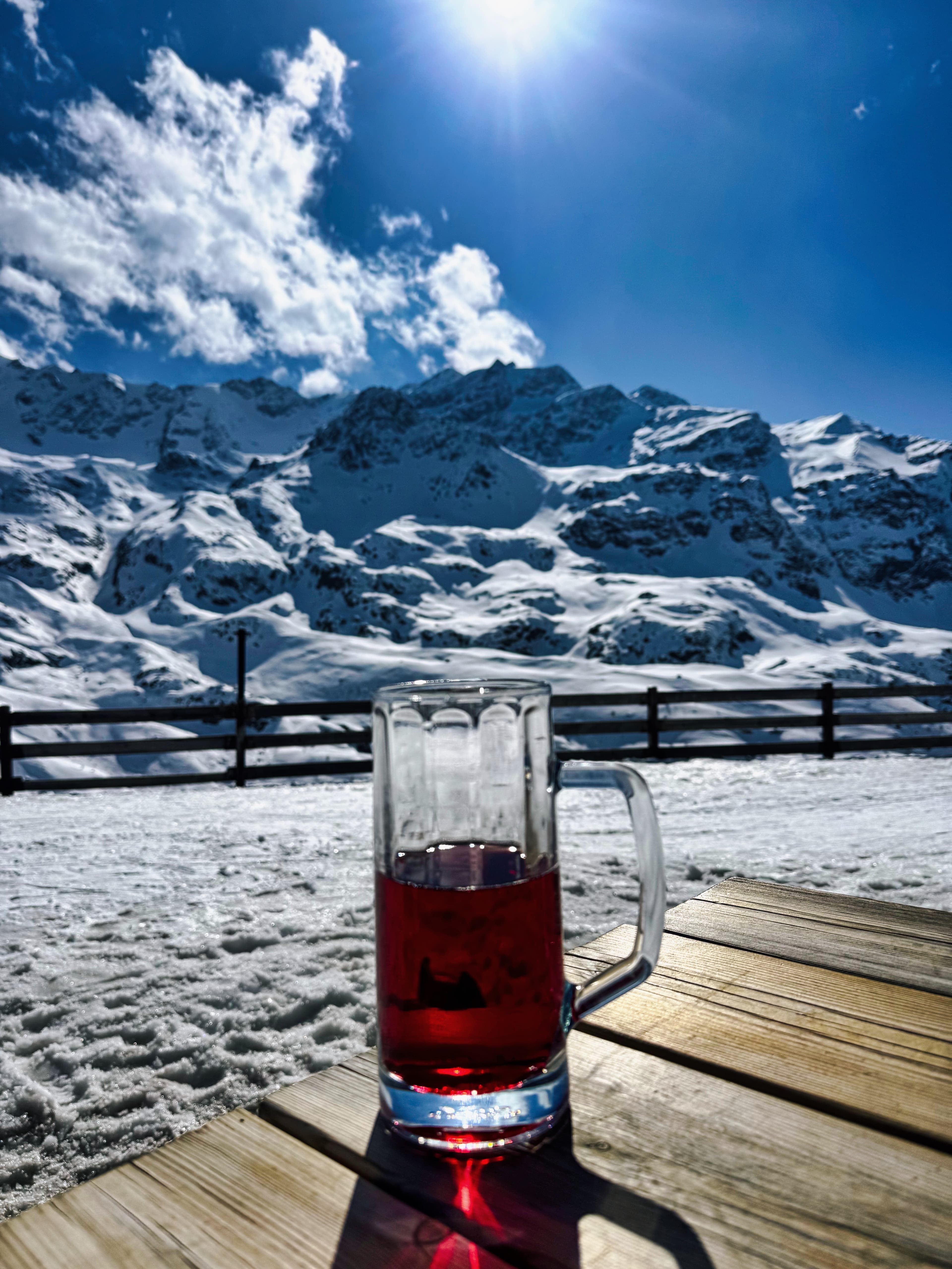 Glass of tea on a wooden table with Ortler mountain panorama behind